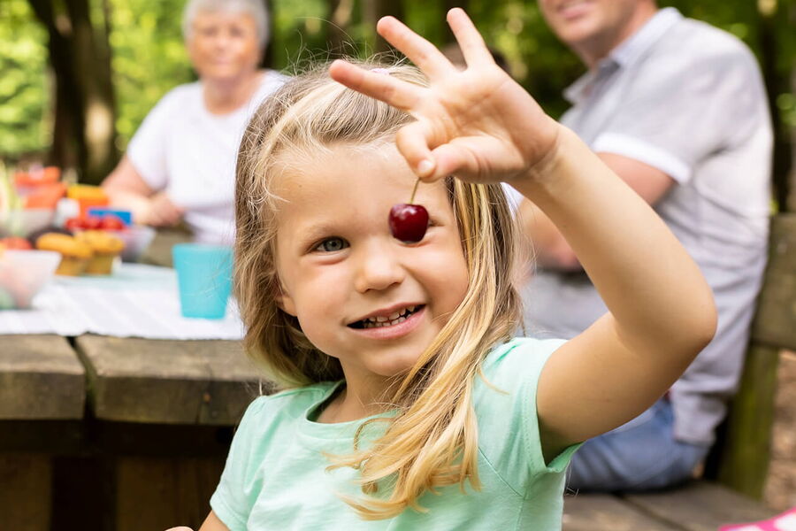 Kleines Mädchen hält Kirsche hoch und hält eine Schale mit Kirschen in der Hand, sie lächelt