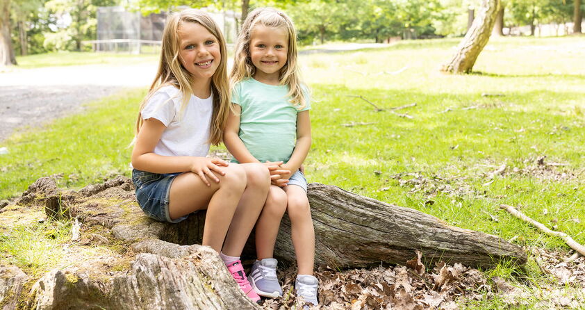 Zwei Mädchen sitzen fröhlich nebeneinander auf einem Baumstamm