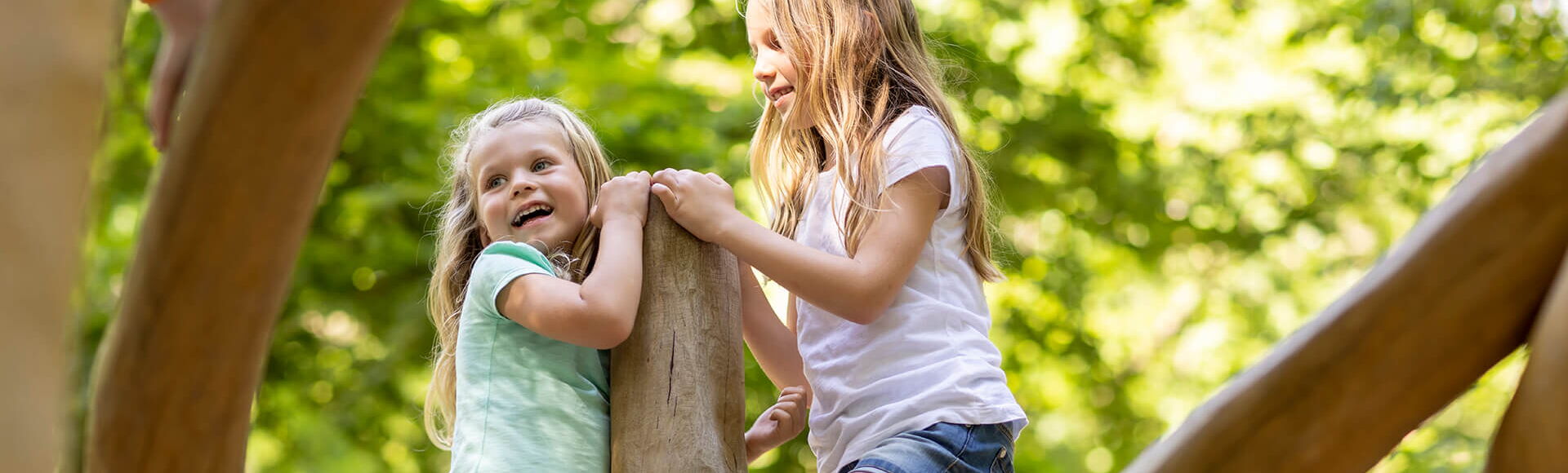 2 Mädchen halten sich an einem Stamm vom Klettergerüst fest